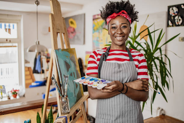 young african artist painting in her home studio, she is looking in camera